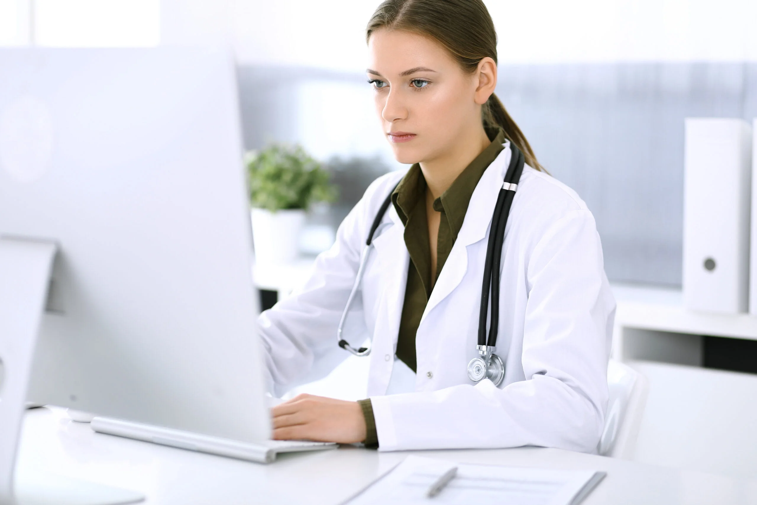 Doctor typing on pc computer while sitting at the desk in hospital office. Physician woman at work. Data in medicine and healthcare.